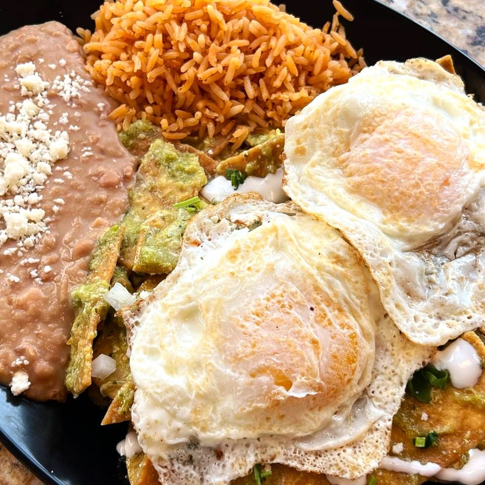 Mexican breakfast plate with refried beans, rice, chilaquiles, and two fried eggs.