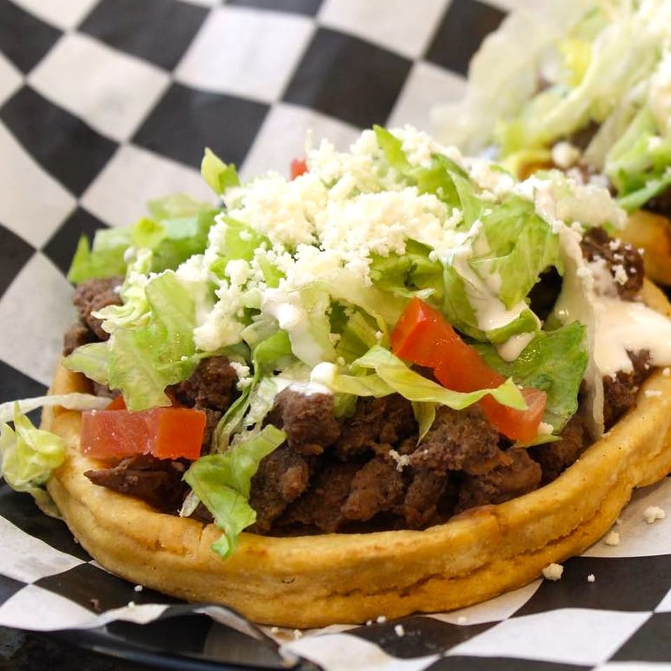 A Boss Man Tacos Burritos & More sopes with meat, lettuce, tomatoes, cheese, and crema.